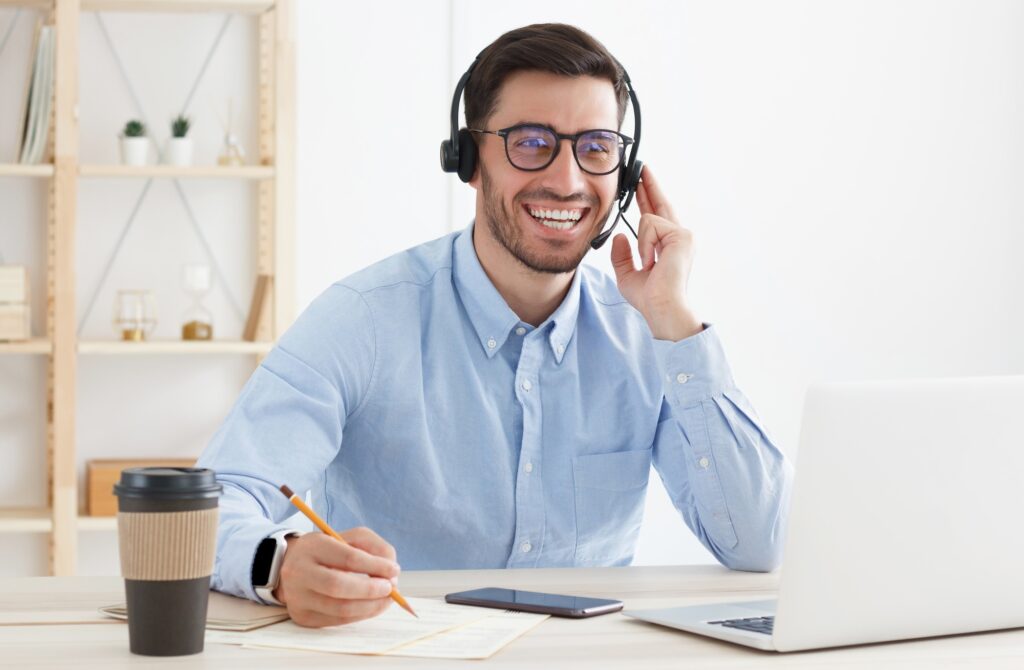 Smiling customer service worker, sitting with laptop at desk in white modern office